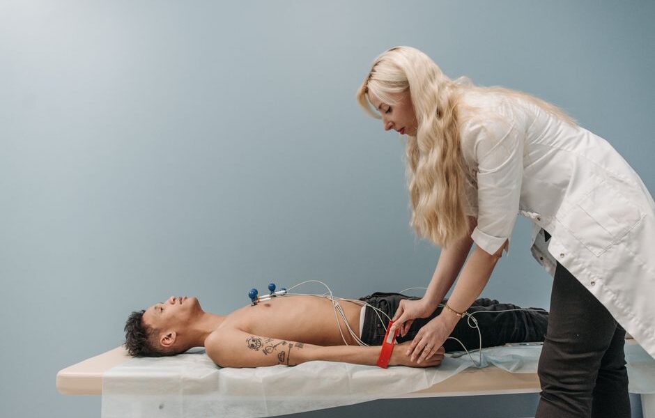 Lekarka zakłada elektrody EKG pacjentowi leżącemu na kozetce w gabinecie lekarskim.