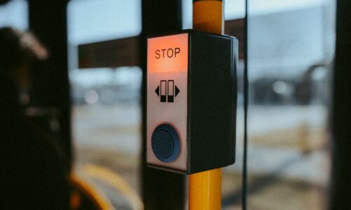 Przycisk stop z podświetleniem w autobusie zamontowany na żółtym słupku.