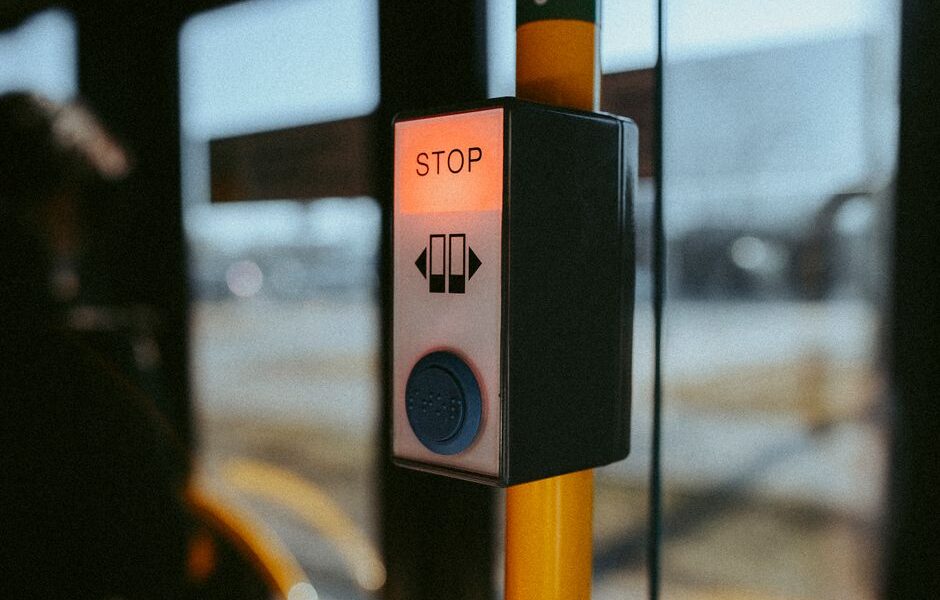 Przycisk stop z podświetleniem w autobusie zamontowany na żółtym słupku.