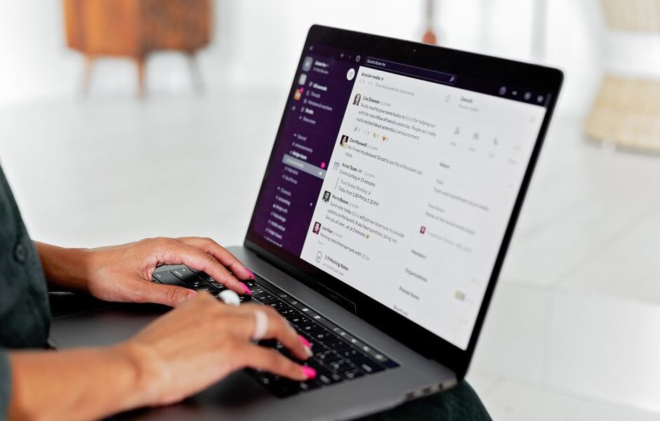 Dłonie piszące na klawiaturze laptopa z otwartą aplikacją do komunikacji zespołowej