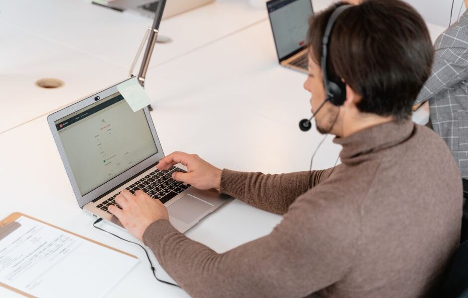 Mężczyzna w słuchawkach z mikrofonem pracuje przy laptopie w biurze