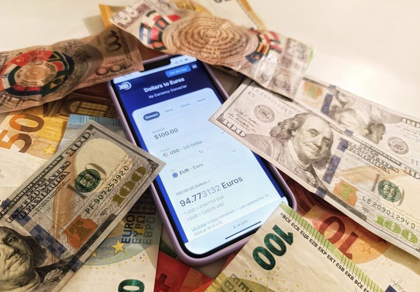 Smartfon z aplikacją do przeliczania walut otoczony banknotami dolarów i euro.