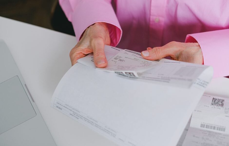Osoba w różowej koszuli trzymająca w dłoniach stos papierowych faktur i paragonów