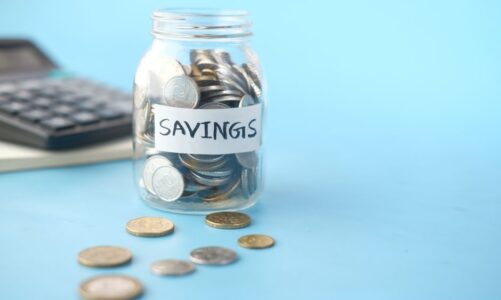 Szklany słoik z monetami i napisem Savings oraz kalkulator w tle