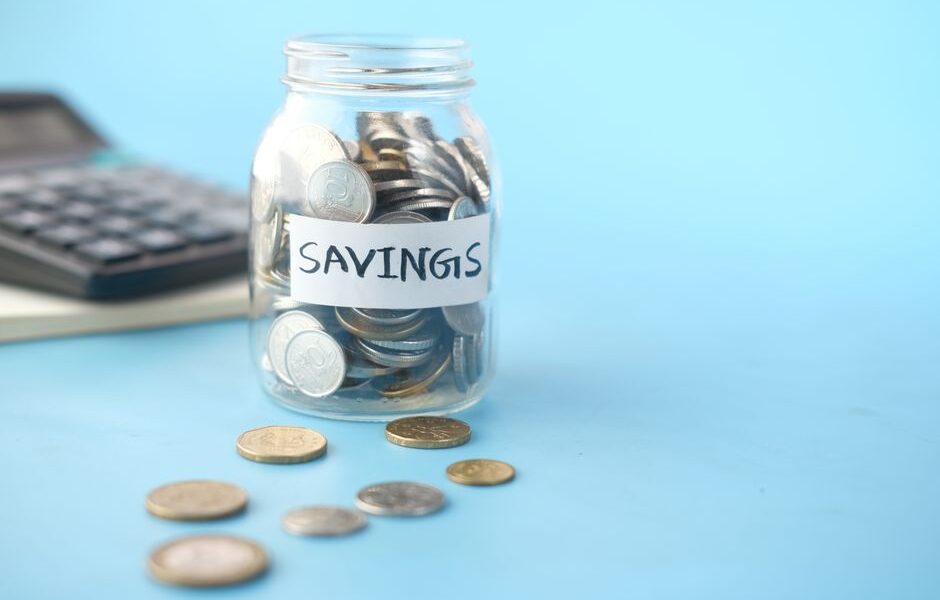 Szklany słoik z monetami i napisem Savings oraz kalkulator w tle