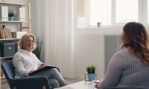 Kobieta w białej koszuli z notatnikiem rozmawia z pacjentką w gabinecie.