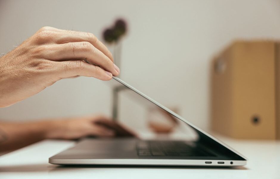 Dłoń zamykająca pokrywę laptopa na biurku.
